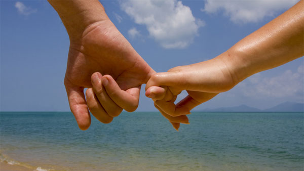 Couple holds hands while walking on the beach.